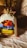 A rustic, textured surface highlights a small burlap sack with a colorful label featuring images of berries and autumn leaves. A box and a ball of twine are positioned in the background, alongside some dried plants.