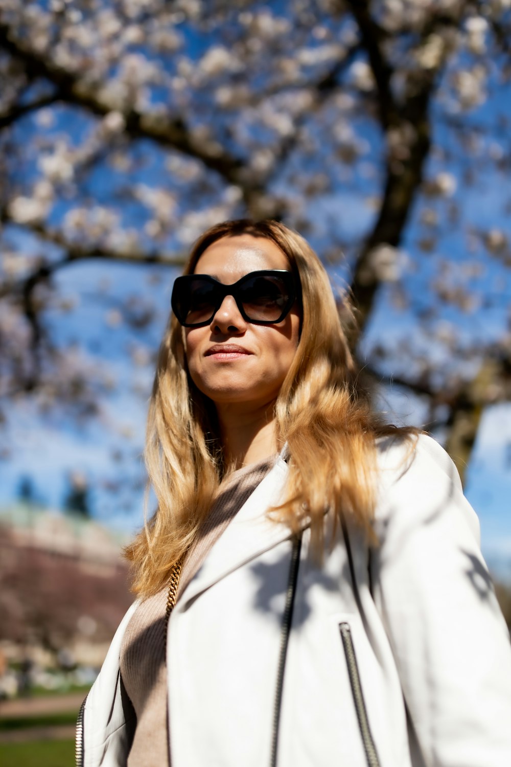 a woman in a white jacket and sunglasses standing in front of a tree