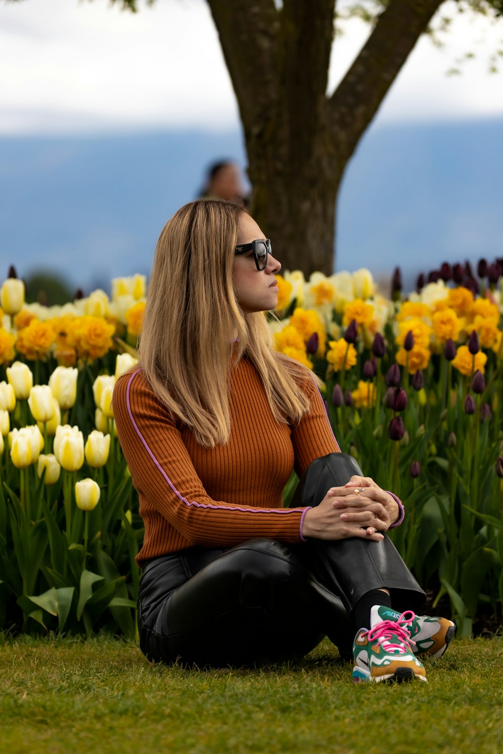 a woman sitting on the ground in front of a field of flowers