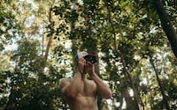 a shirtless man taking a selfie in the woods