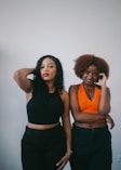 Photo of a Latina nurse practitioner and a Black nurse practitioner with natural hair, both in scrubs, standing together in a bright clinic hallway.