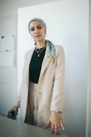 A woman in a minimalist co-ord set standing against an off-white wall, radiating quiet confidence.