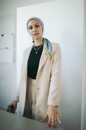 Elegant portrait of Yasmin in a sophisticated navy blazer, standing in a modern luxury home with beige and gold accents.