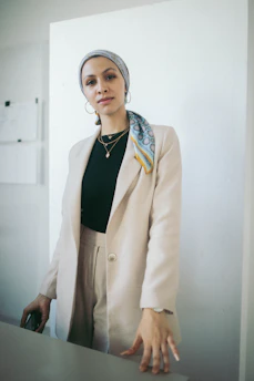 A chic model in a cream silk blouse and tailored beige trousers, standing against a minimalist ivory backdrop with soft gold accents.