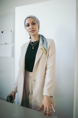 Elegant portrait of Yasmin in a sophisticated navy blazer, standing in a modern luxury home with beige and gold accents.
