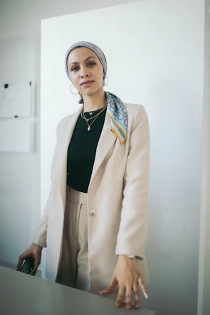 Close-up of a layered outfit featuring neutral tones with a pop of beige accessories against a white wall.