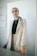 A sophisticated woman wearing a tailored blazer, standing in a softly lit minimalist room.