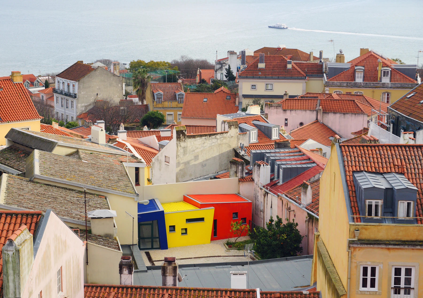 Terracotta rooftops and colorful residential buildings overlooking the waterfront in Lisbon, Portugal.