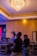 Two people are using professional video equipment in a venue with a large chandelier and various technical equipment around. The setting suggests preparation or coverage for an event.