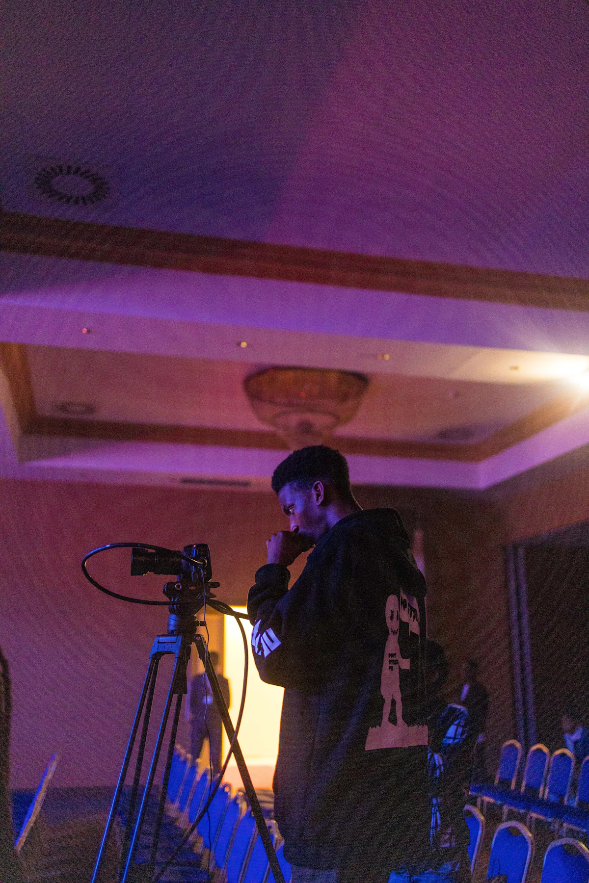 A creator filming with a camera on a tripod in a purple-lit venue