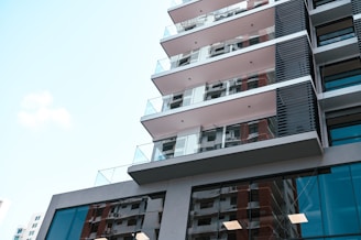 Facade of a sleek apartment tower with glass balconies and shops below.