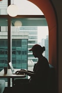 A stylish young Asian professional woman confidently working on a laptop in a modern office with vibrant cityscape background