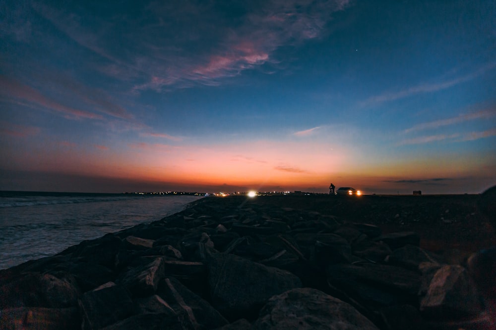 the sun is setting over the ocean with rocks in the foreground