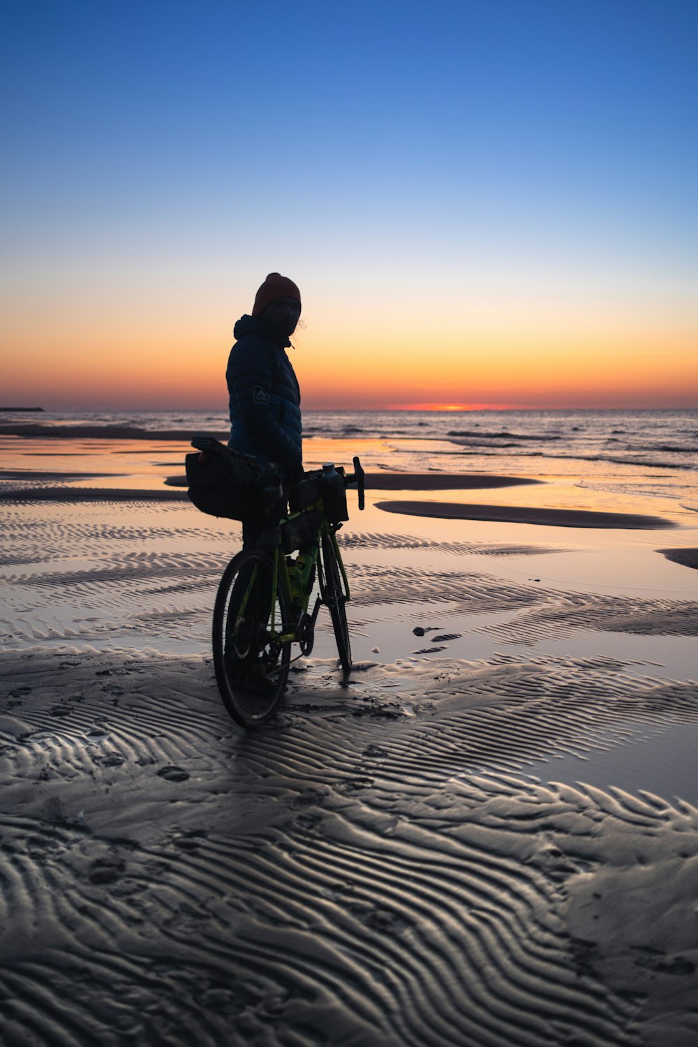 a person riding a bike on a beach at sunset