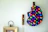 A wall features decorative elements including a patterned cloth or bag adorned with colorful hearts and rainbow designs, hanging on rustic wooden pegs. A framed object below shares the space, adding a vintage touch with its minimalistic frame and faded photograph.