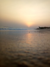 View of a quiet beach with gentle waves and a boat floating nearby at sunset.