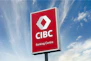 A large outdoor sign with a red background displaying the logo and text of a banking center, set against a partly cloudy blue sky.