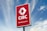 A large outdoor sign with a red background displaying the logo and text of a banking center, set against a partly cloudy blue sky.