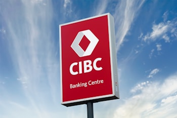 A large outdoor sign with a red background displaying the logo and text of a banking center, set against a partly cloudy blue sky.