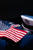 An American flag is displayed on a dark navy blue military uniform adorned with service medals. The uniform includes a white peaked cap featuring an eagle emblem.
