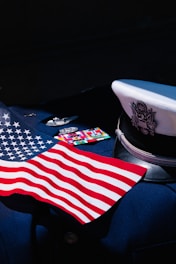 An American flag is displayed on a dark navy blue military uniform adorned with service medals. The uniform includes a white peaked cap featuring an eagle emblem.