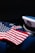 An American flag is displayed on a dark navy blue military uniform adorned with service medals. The uniform includes a white peaked cap featuring an eagle emblem.