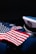 An American flag is displayed on a dark navy blue military uniform adorned with service medals. The uniform includes a white peaked cap featuring an eagle emblem.