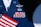 A military uniform with various colorful ribbons and medals displayed on it, accompanied by a small American flag. The uniform is dark blue with metallic badges indicating rank and service.