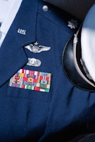 A formal military uniform featuring a collection of service ribbons, pins, and insignia on a navy blue coat. Visible is a white peaked cap with a black visor beside it. The uniform displays symbols of rank and recognition.