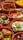 Various earthenware dishes filled with an assortment of Middle Eastern or Mediterranean foods including sliced tomatoes and cucumbers, falafel, creamy dips with herbs, olives, and pickles. Each dish is arranged attractively with garnishes of mint and other herbs.