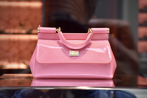 A close-up of a pastel pink handbag with delicate gold accents on a marble countertop.