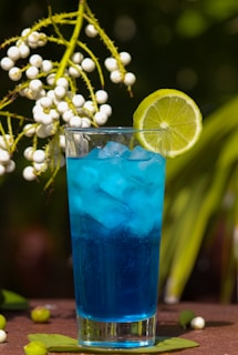 A chilled glass filled with a bright blue cyan beverage with ice cubes and a straw.