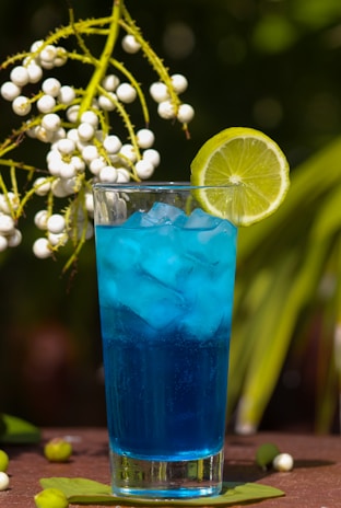 A chilled glass filled with a bright blue cyan beverage with ice cubes and a straw.