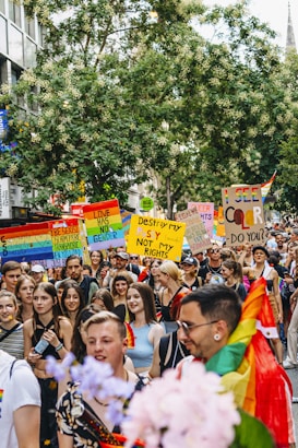 A lively and colorful parade with multiple people holding signs advocating for LGBTQ+ rights and equality. The crowd is diverse, with rainbow flags and vibrant outfits, contributing to a festive and inclusive atmosphere.