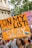 A vibrant protest scene featuring people holding signs advocating for LGBTQ+ rights. The focal point is a large orange sign with the text 'On My Gay List: Slay' in bold letters. The crowd is colorful and engaged, with participants displaying symbols of pride, such as rainbow flags.