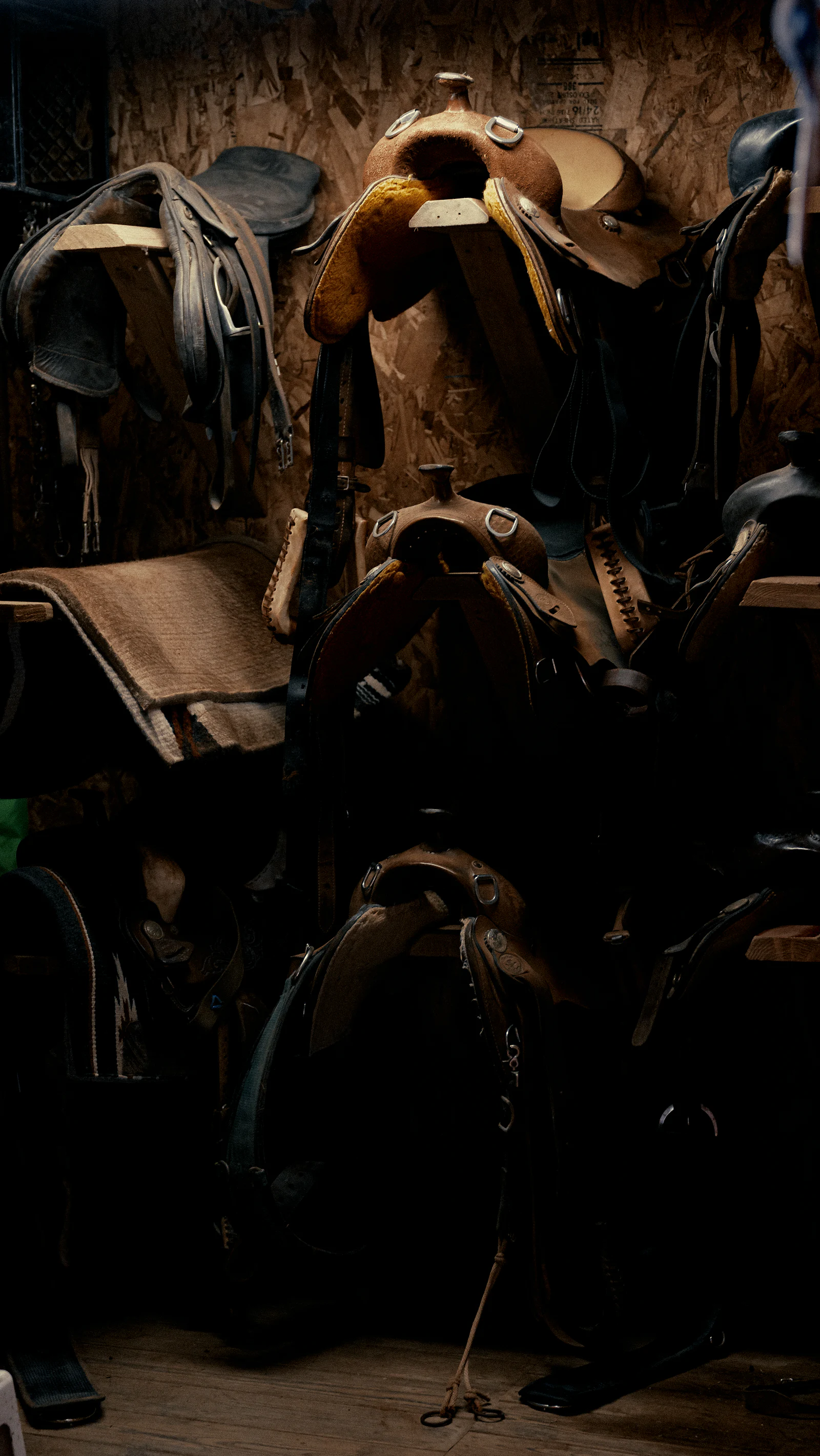 A stack of worn leather saddles resting on a wooden floor.