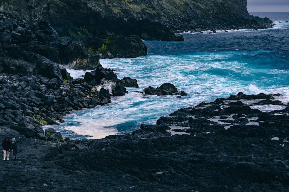 a couple of people standing on top of a rocky beach