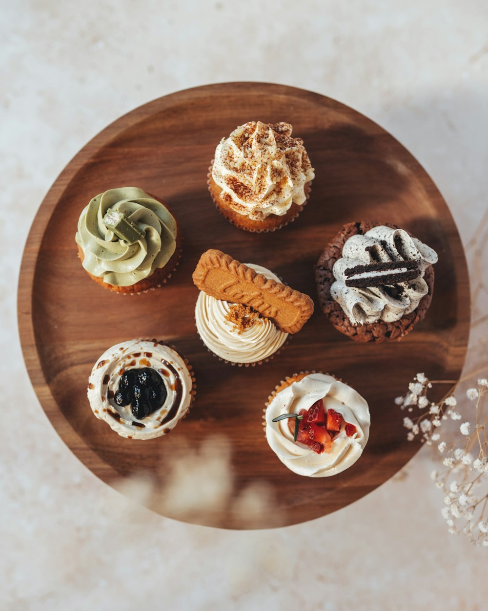 a wooden plate topped with different types of cupcakes