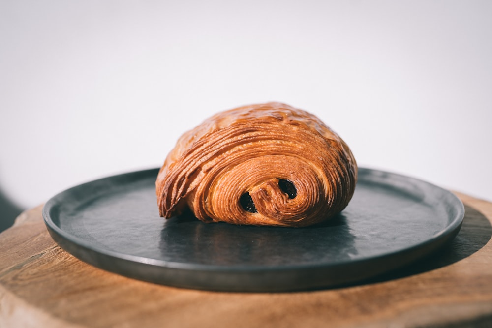 a croissant on a black plate on a wooden table