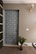 A modern interior door with a woven pattern design positioned next to a ribbed beige wall. There is a small potted plant at the base of the wall and a light fixture with a decorative bulb mounted above. The area has a carpeted floor and a light switch is visible on the wall.