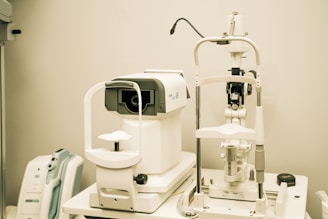 A set of ophthalmic diagnostic equipment, including an autorefractor and a slit lamp, arranged in a medical examination room with a beige backdrop. The machines are white with various dials and functional parts visible.