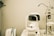A white optometry machine is situated on an examination table, used for eye testing, alongside other medical equipment in a clinical setting. The background is neutral with smooth walls.