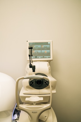A medical device is positioned against a plain background. The machine features a screen displaying various icons and controls, likely for diagnostic purposes, and an apparatus for eye examination.