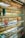 Several shelves display a variety of colorful eyeglasses against a brick wall, with each shelf showcasing different colors such as red, orange, yellow, blue, and purple. Small portrait photos are placed intermittently among the glasses.