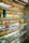 Several shelves display a variety of colorful eyeglasses against a brick wall, with each shelf showcasing different colors such as red, orange, yellow, blue, and purple. Small portrait photos are placed intermittently among the glasses.