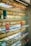 Several shelves display a variety of colorful eyeglasses against a brick wall, with each shelf showcasing different colors such as red, orange, yellow, blue, and purple. Small portrait photos are placed intermittently among the glasses.