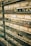 Multiple pairs of eyeglasses are neatly displayed on glass shelves against a brick wall. The glasses vary in style, shape, and color, creating a visually appealing array.