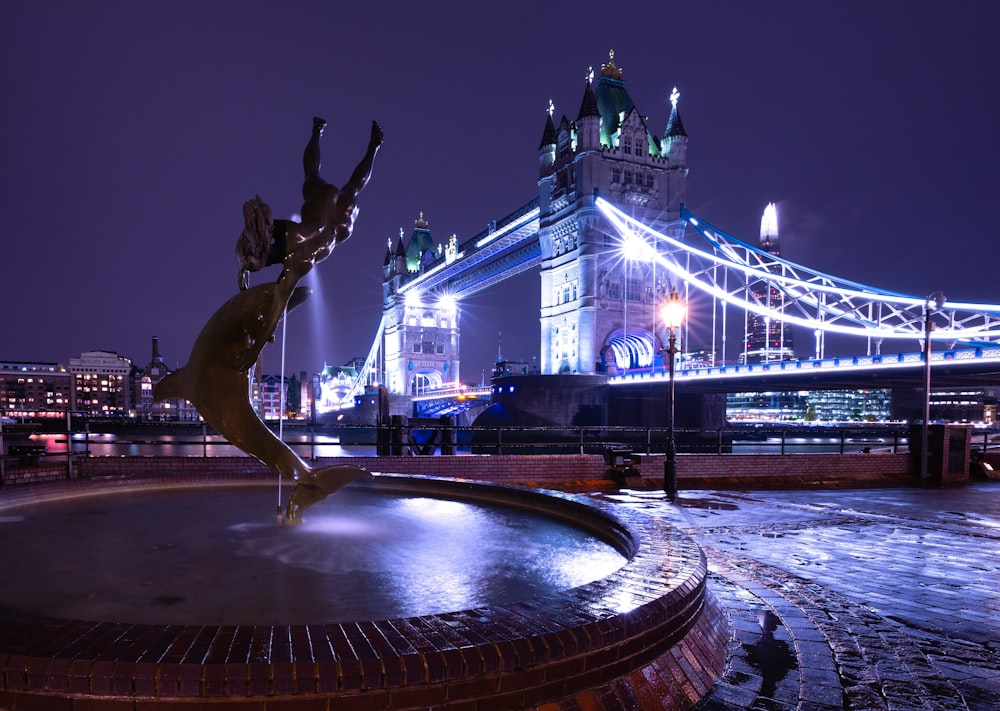 a statue in front of the tower bridge at night