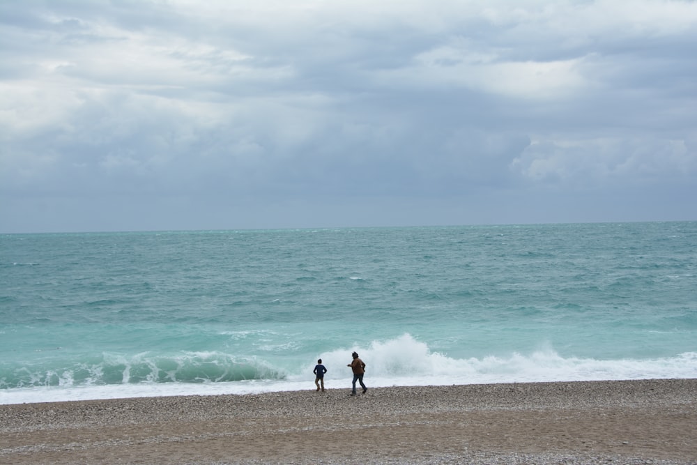 a couple of people standing on top of a sandy beach