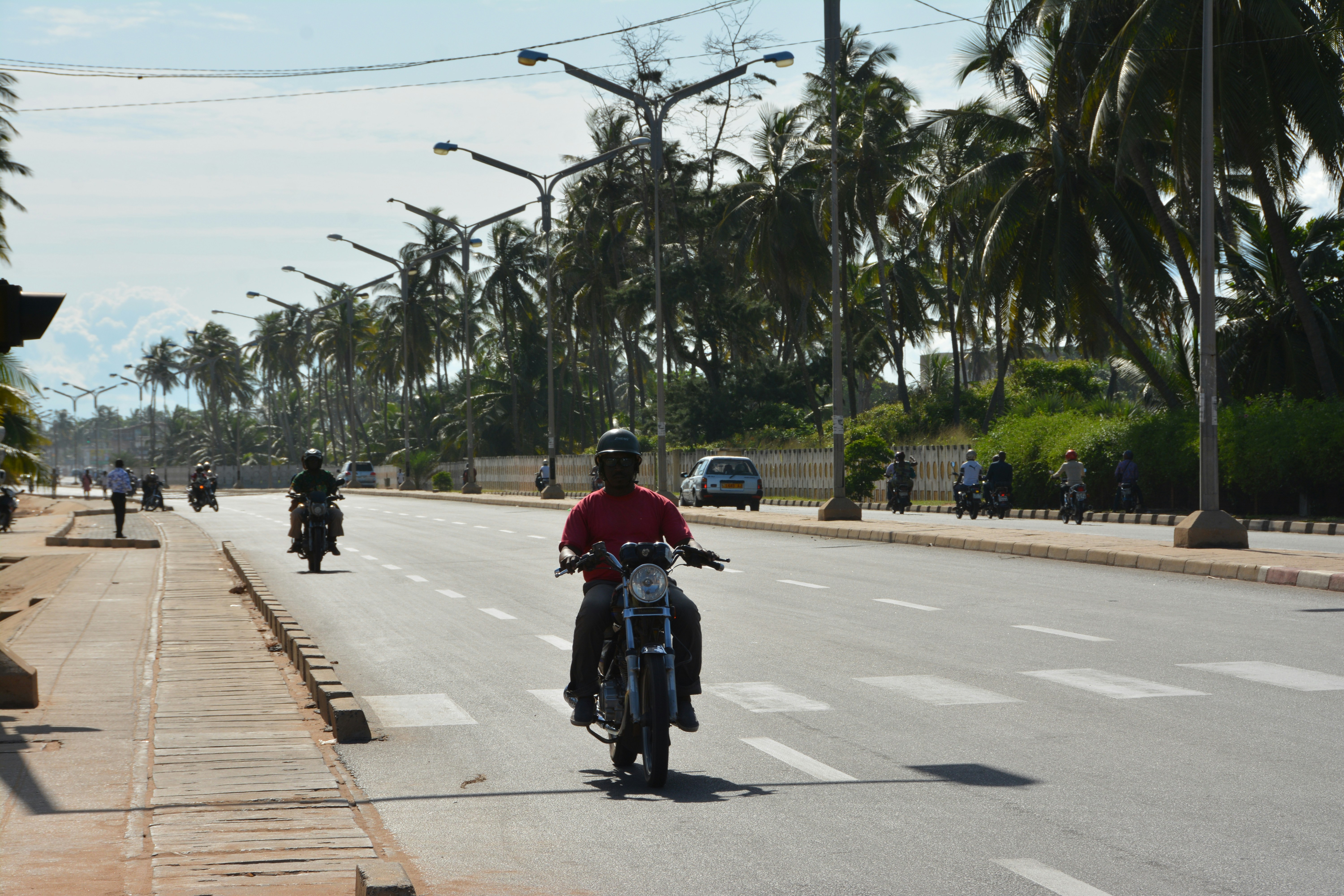 a man riding a motorcycle down a street next to palm trees, 